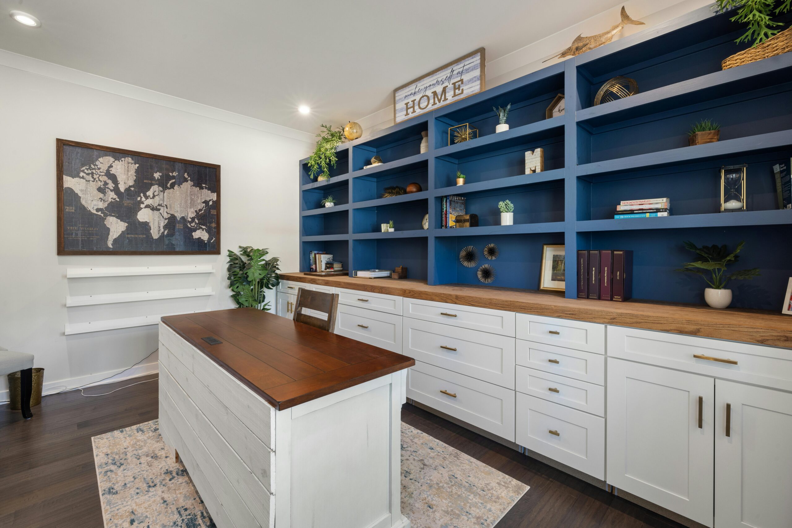 Modern home office featuring blue shelves with decor, a wooden desk, and world map artwork.